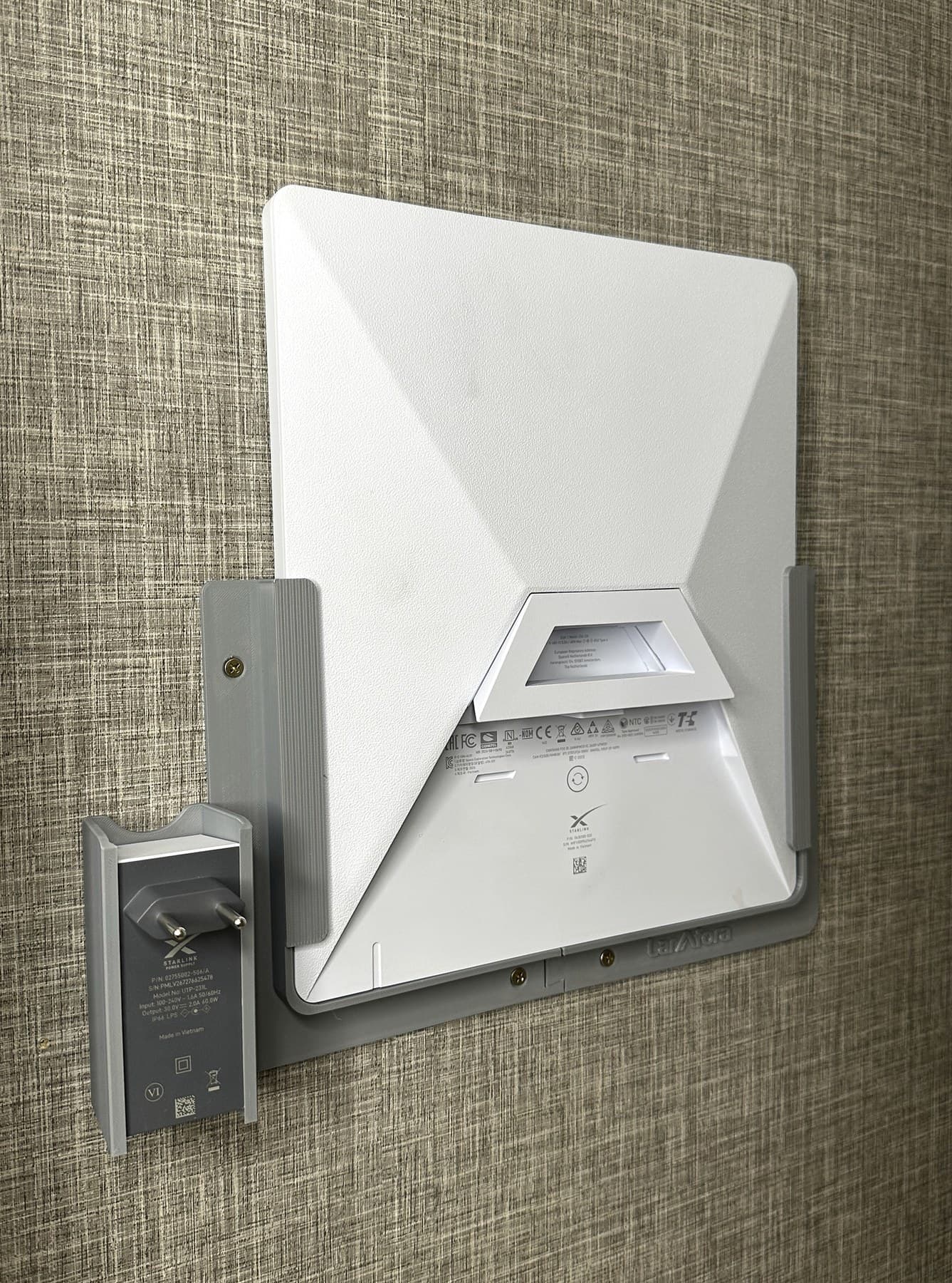 Demonstração dos suportes cinza instalados na parede com antena Starlink Mini e fonte.